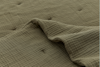 Close-up of a textured, olive green quilt with a wavy, grid-like pattern. Part of the quilt is gently folded over, revealing the soft, plush surface and subtle stitching details.