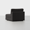 A modern, dark gray upholstered armless chair with clean lines and a boxy shape sits on a light gray floor against a plain white background.