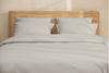 A neatly stacked set of light gray bed sheets and pillowcases arranged on top of each other against a white background.