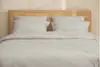 A neatly stacked set of light gray bed sheets and pillowcases arranged on top of each other against a white background.