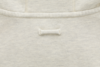 Close-up of a light beige sweatshirt, focusing on a small, horizontal loop of fabric stitched below the neckline. The material appears soft and textured, with visible stitching details.