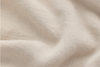 A close-up of beige linen fabric shows a soft, slightly wrinkled texture with visible weave patterns and gentle folds throughout the material.
