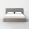 A modern, minimalist bed with a light wood frame, gray upholstered headboard, and white bedding, positioned against a plain white wall on a light gray floor.