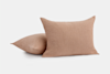 Two light brown, textured rectangular pillows are placed on a plain white background, with one pillow standing upright and the other lying flat behind it.