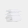 Two white pillows are stacked on top of a neatly folded white comforter, all set against a plain white background.