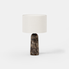 A table lamp with a cylindrical marble base in dark brown tones and a round, white fabric lampshade, set against a plain white background.