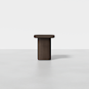 A minimalist, dark brown wooden pedestal table with a rectangular top and a solid cylindrical base, set against a plain white background.