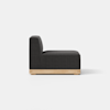 A modern armless black upholstered chair with a tall back and thick seat cushion, featuring a light wooden base, viewed from the side against a plain white background.