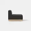 A modern armless black upholstered chair with a tall back and thick seat cushion, featuring a light wooden base, viewed from the side against a plain white background.