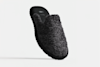 A single dark gray, fuzzy slipper with a closed toe and open back is displayed on a plain white background, slightly tilted to show the textured material and black sole.