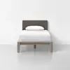 A minimalist single bed with a brown upholstered headboard, white bedding, and a single white pillow, set against a plain white wall and floor.