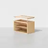 A light wood storage box with an open front and one internal shelf, shown with its flat lid lifted above it, positioned on a smooth grey floor against a plain white background.