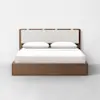 A modern wooden bed with a rectangular, upholstered headboard, two white pillows, and white bedding, set against a plain white wall and gray floor.