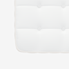 Close-up of a white, tufted mattress corner showing four button tufts and stitched edges against a plain white background.