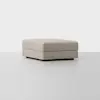 A large, square, light beige ottoman with clean lines and a minimalist design, placed on a light gray floor against a plain white background.