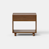 A modern wooden nightstand with a single drawer and an open lower shelf, standing on four short cylindrical legs. The design is minimalist with clean lines, and the wood has a smooth, medium-brown finish.