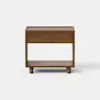 A modern wooden nightstand with a single drawer and an open lower shelf, standing on four short cylindrical legs. The design is minimalist with clean lines, and the wood has a smooth, medium-brown finish.