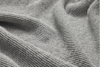 Close-up of a textured, light gray knitted fabric with a waffle weave pattern, showing gentle folds and soft shadows.