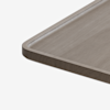 A close-up of the corner of a rectangular wooden tray with rounded edges and a shallow lip, set against a plain white background.