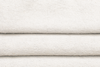 Close-up of neatly folded, off-white textured fabric with a subtle woven pattern, showing slight variations in thickness and gentle shadows between the folds.