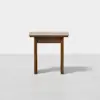 A small, square wooden side table with clean lines and a simple, minimalist design, standing on a light, plain surface against a white background.