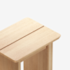 A close-up of a light wood table or bench with a smooth finish and a narrow gap running lengthwise down the center of the surface.