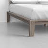 Close-up of a modern wooden bed frame with a light gray finish, featuring clean lines and sturdy legs, topped with a neatly made bed and white bedding in a minimalistic room.