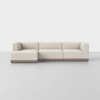 A modern L-shaped sectional sofa with light beige upholstery and a wooden base, placed on a smooth, light gray floor against a plain white background.