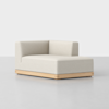 A modern, minimalist beige chaise lounge with low wooden base and right-angle backrest, positioned on a light gray floor against a plain white background.