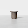 A minimalist, square-topped side table with rounded edges and a solid cylindrical base, made of light brown wood, is placed on a plain, light gray background.