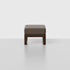 A minimalist ottoman with a dark wooden base and a rectangular, light brown cushioned top, set against a plain white background.