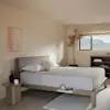 A minimalist bedroom with a light wood bed, white bedding, two pillows, a bedside table with a vase and candle, a potted plant, a shelf with books, a window with a mountain view, and a soft neutral color palette.