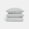 Two light grey pillows stacked on top of a folded matching quilt or comforter, all with a subtle square stitched pattern, set against a plain white background.