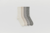 Four pairs of crew-length socks in different neutral colors—cream, light beige, light gray, and dark gray—are neatly arranged side by side on a plain white background.