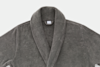 A close-up of a gray, plush bathrobe with a shawl collar, displayed on a white background. The robe appears soft and cozy, with a visible brand tag at the neck.