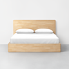 A wooden bed frame with a light finish, featuring a simple rectangular headboard and two white pillows, with white bedding, set against a plain white wall and gray floor.