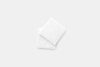 Two white, square washcloths are stacked slightly askew on a plain, light gray background.