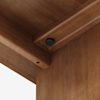 Close-up view of the underside corner of a wooden table or desk, showing the joint where two panels meet and a black screw or fastener securing the connection.