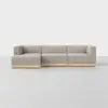 A modern, light gray sectional sofa with clean lines and a low wooden base, set against a plain white background on a smooth, light-colored floor.