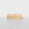 A minimalist wooden dresser with four drawers, placed on a light gray floor against a plain white background. The dresser has a smooth, natural finish and a simple, modern design.