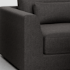 A close-up view of the arm and seat of a dark gray upholstered sofa, showing its textured fabric and modern, boxy design.