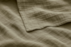 A close-up of a soft, beige fabric with a subtle grid pattern, showing gentle folds and a neatly finished edge.