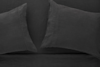 Two dark gray linen pillows rest on a matching dark gray linen bed sheet, creating a monochromatic and minimalist bedding arrangement.