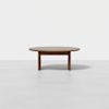 A round wooden coffee table with a smooth surface and three sturdy legs, set against a plain white background.