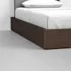 A close-up view of a modern bed with a dark wooden frame, white bedding, and a light grey headboard, set on a light-colored floor against a white wall.