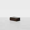 A dark brown wooden rectangular box sits alone on a smooth, light gray floor against a plain white background.