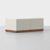 A modern, modular beige sofa with clean lines and a low wooden base, set against a plain white background, viewed from the back and slightly to the side.