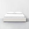 A minimalist bed with a light beige upholstered frame, two white pillows, and a neatly made white duvet, set against a plain white wall and gray floor.