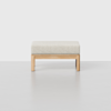 A minimalist wooden stool with a light beige cushioned seat, set against a plain white background.