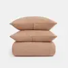 Two beige, textured pillows are stacked on top of a matching folded blanket, all with a crinkled fabric appearance, against a plain white background.